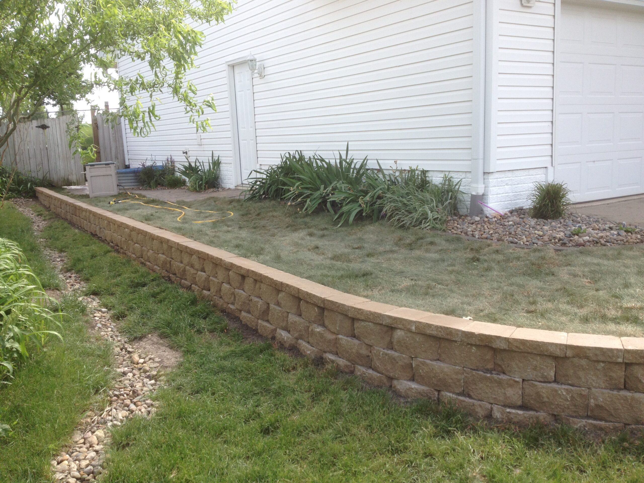 Curved stone retaining wall with landscaped garden and grass area, illustrating outdoor design principles for family-friendly spaces.