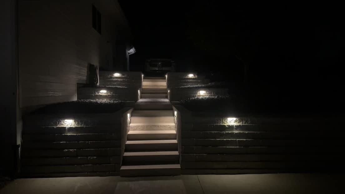 Illuminated outdoor staircase leading to a house at night, featuring modern lighting design, emphasizing landscaping and outdoor aesthetics.