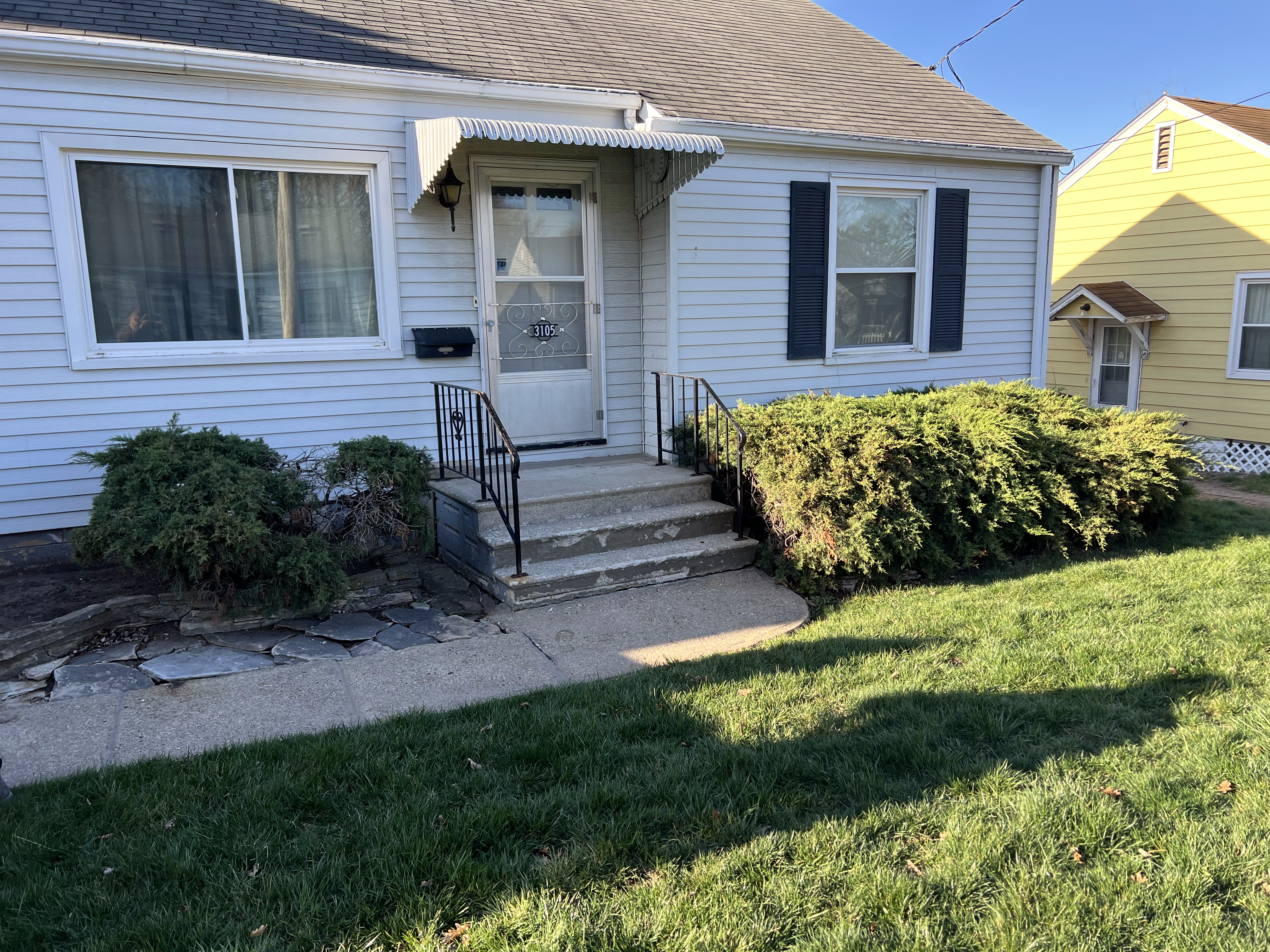 Front entry landscape of a residential home in Des Moines, featuring stone pathway, shrubs, and a welcoming porch with a door, illustrating essential landscaping elements for enhancing curb appeal.