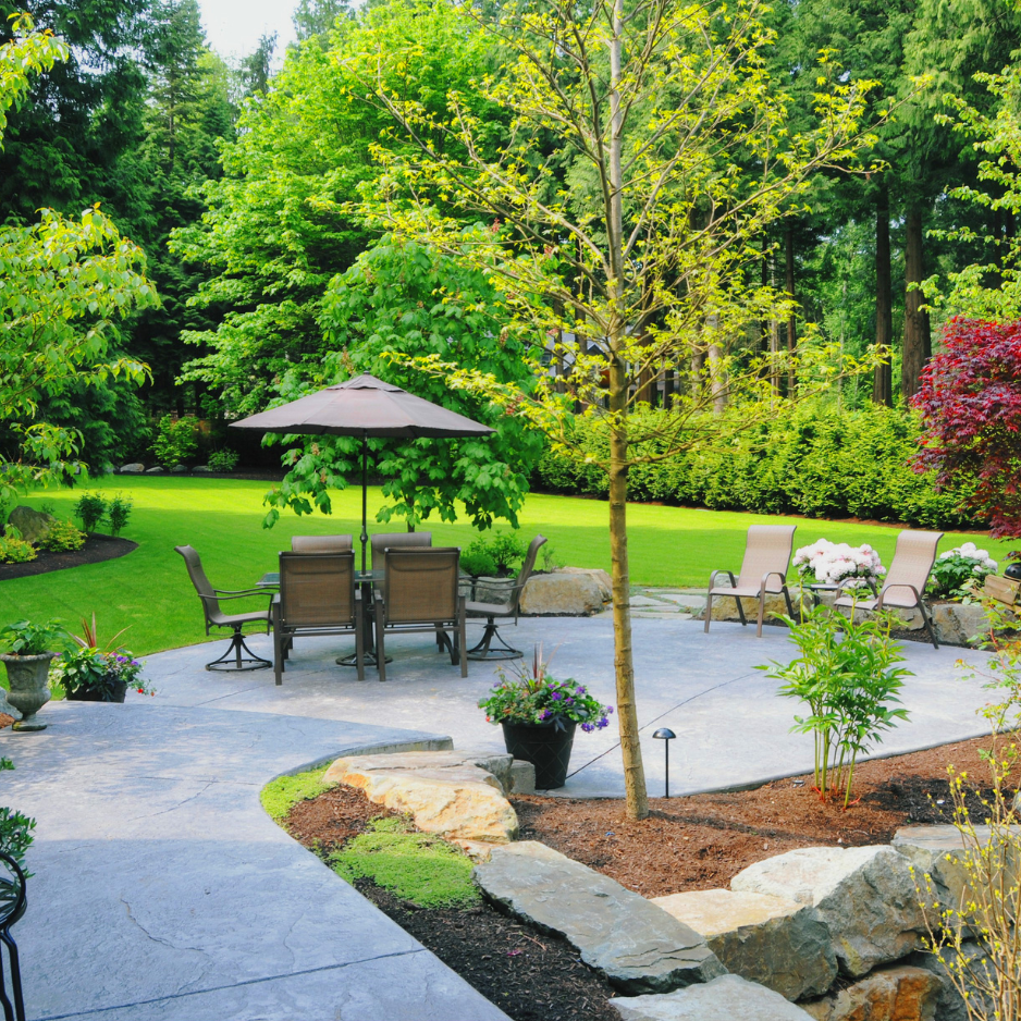 Cozy outdoor seating area with a table and umbrella, surrounded by lush greenery and landscaped garden, perfect for family-friendly gatherings and relaxation.