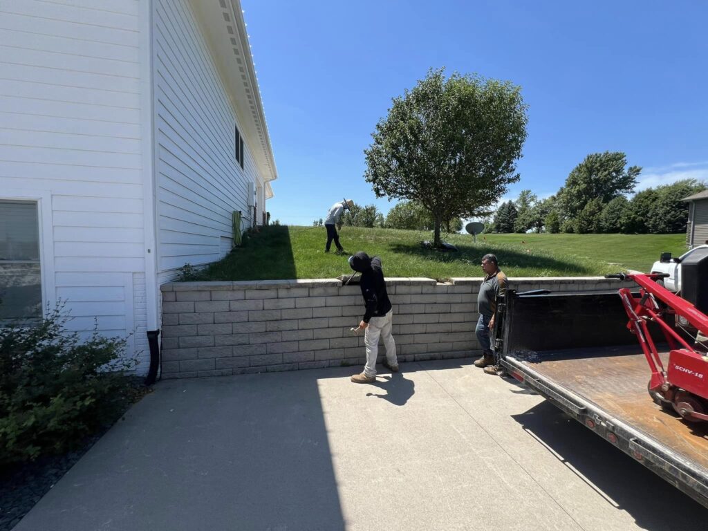 Two landscaping professionals working near a retaining wall, with a green lawn and trees in the background, showcasing landscape planning and design services in Des Moines.