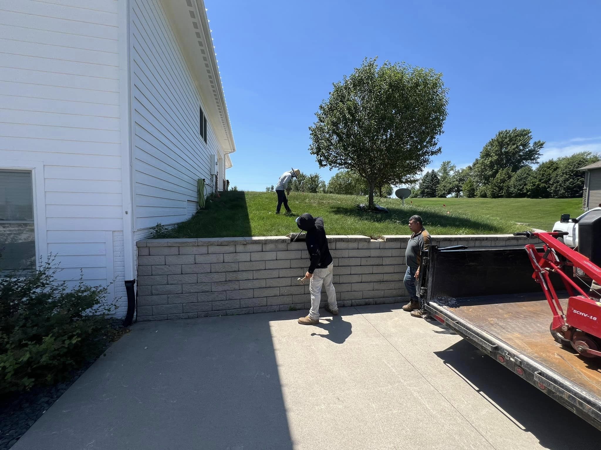Workers collaborating on landscaping project, featuring a retaining wall, grassy area, and a truck with equipment, emphasizing outdoor living space enhancement in Des Moines.