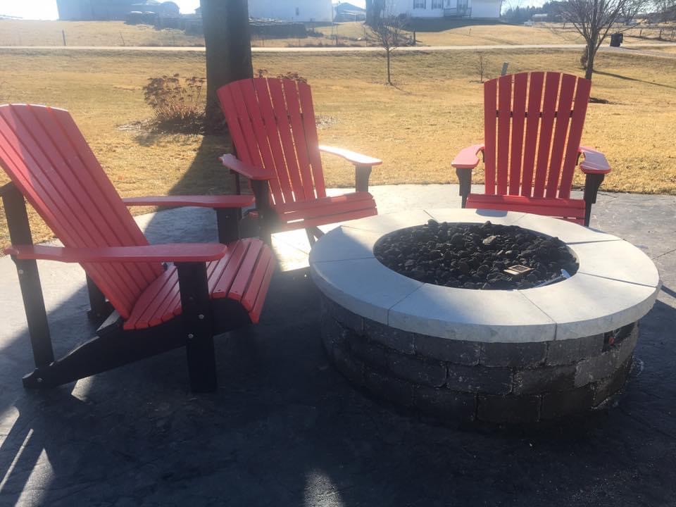 Red Adirondack chairs surrounding a stone fire pit on a patio, enhancing outdoor space for year-round gatherings in Altoona.