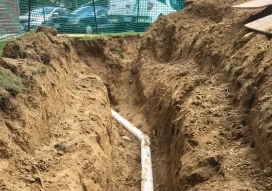 Trench for drainage installation with exposed white pipe, surrounded by freshly dug soil, illustrating yard layout adjustments for improved water flow management.