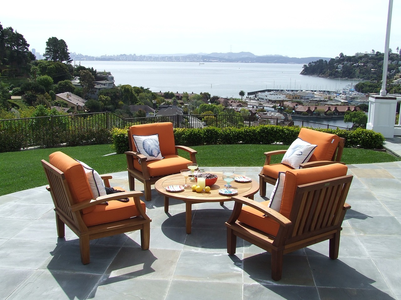 Outdoor patio with orange cushioned chairs and a round table, overlooking a scenic waterfront view, ideal for enhancing backyard functionality and aesthetics in landscaping.